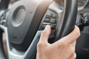 Cropped image of a hand pushing control buttons on steering wheel in a modern car. Driver hand. Test drive